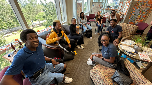 A group of eight college students sit in a circle in an office and talk about issues affecting them.