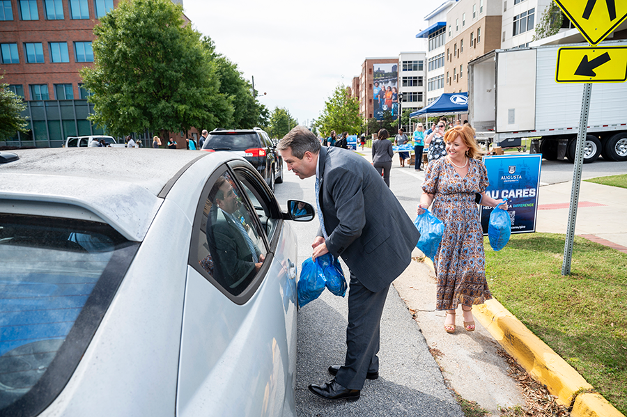 A man and a woman hand out bags of food to people in cars.