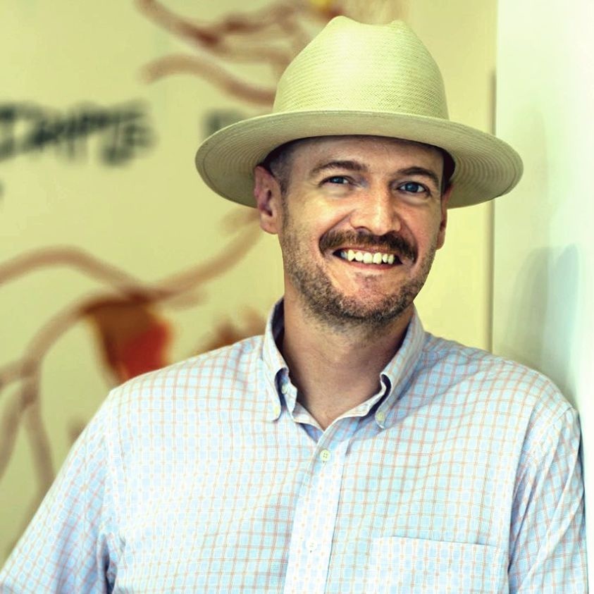 Man wearing a straw hat smiles in a gallery