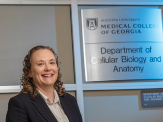 A woman stands next to a plaque that reads Augusta University Medical College of Georgia Department of Cellular Biology and Anatomy