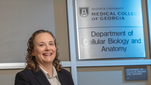 A woman stands next to a plaque that reads Augusta University Medical College of Georgia Department of Cellular Biology and Anatomy