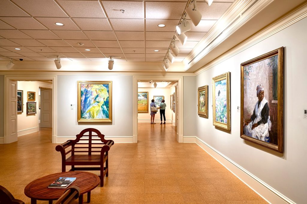 Two women stand in a back exhibition room in a museum looking at a painting.