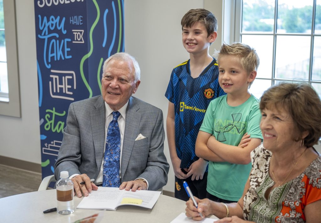 An author poses for a photo with two children while signing a book.