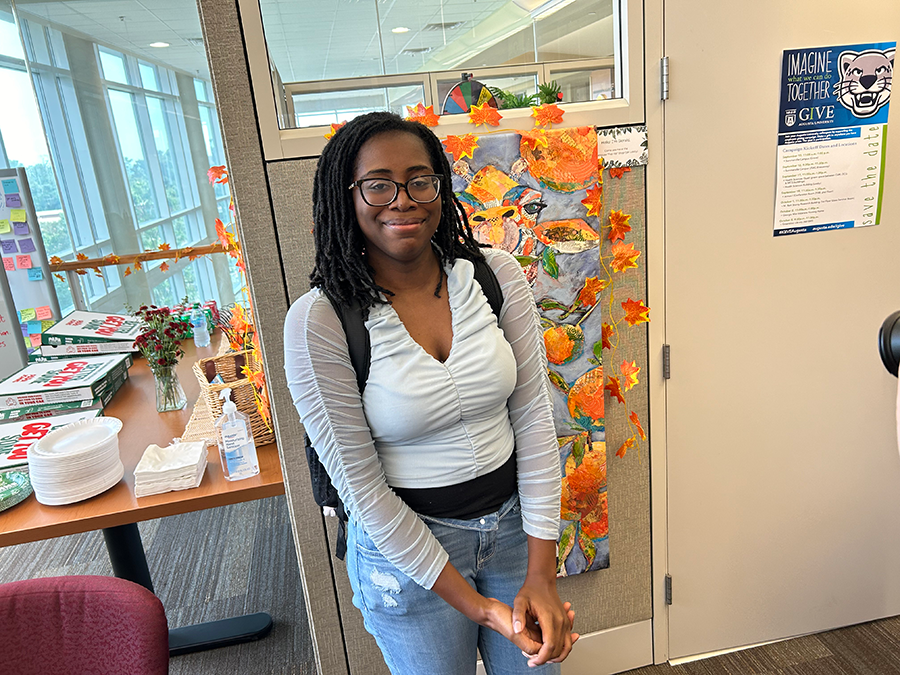 A female college student stands in an office area.