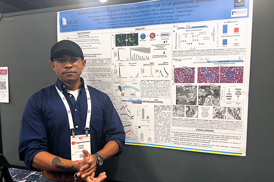 A man stands in front of a large scientific poster detailing his research on nicotine exposure.