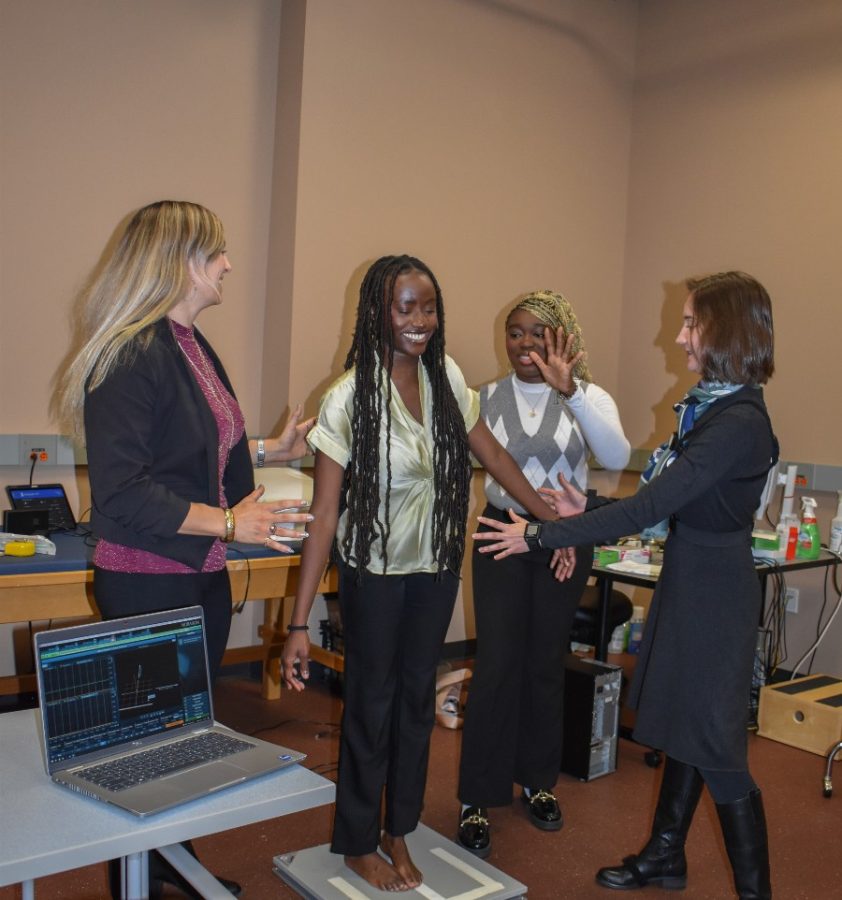 A female professor and two students make sure a student on a force platform doesn't fall off.