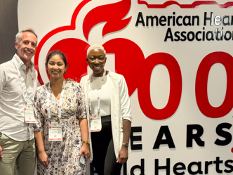 Two women and a man stand in front of a large sign for the American Heart Association.