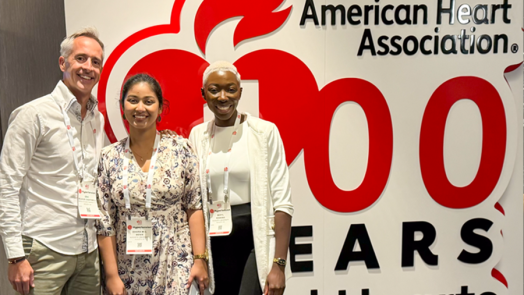 Two women and a man stand in front of a large sign for the American Heart Association.