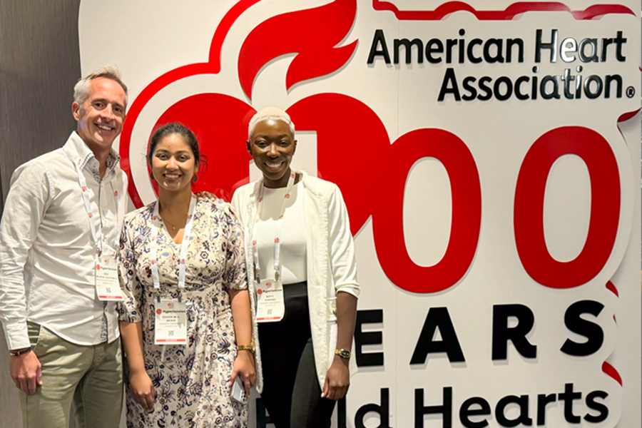 Two women and a man stand in front of a large sign for the American Heart Association.