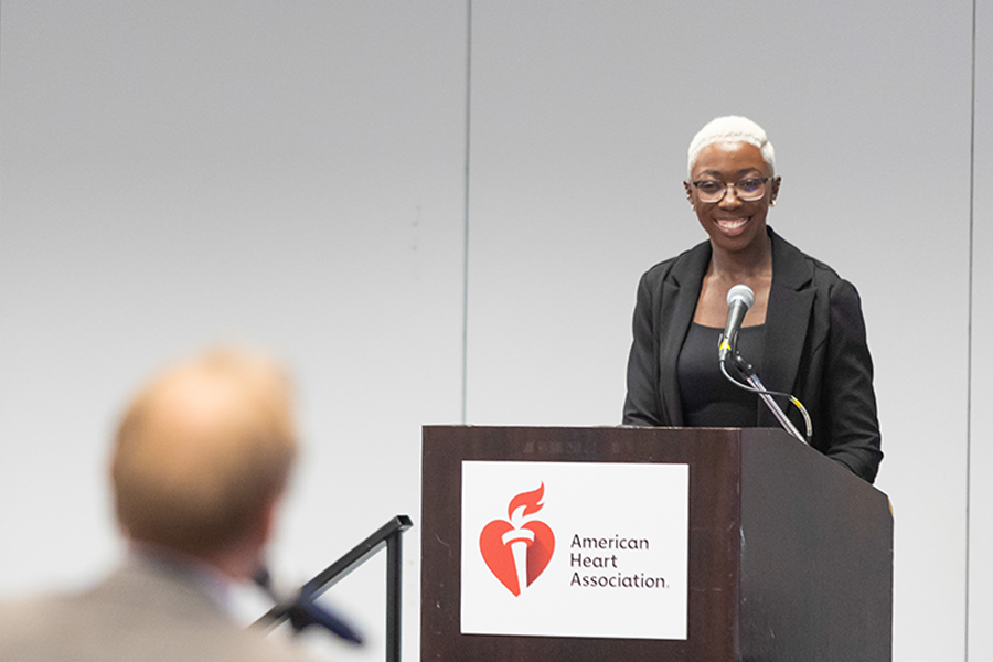 A woman stands at a podium in front of a large lecture hall and answers a question from the crowd.