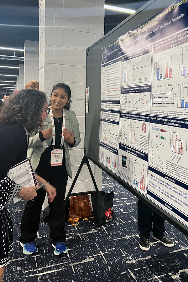 Two women look at a large poster presentation of scientific findings in a large lecture hall.