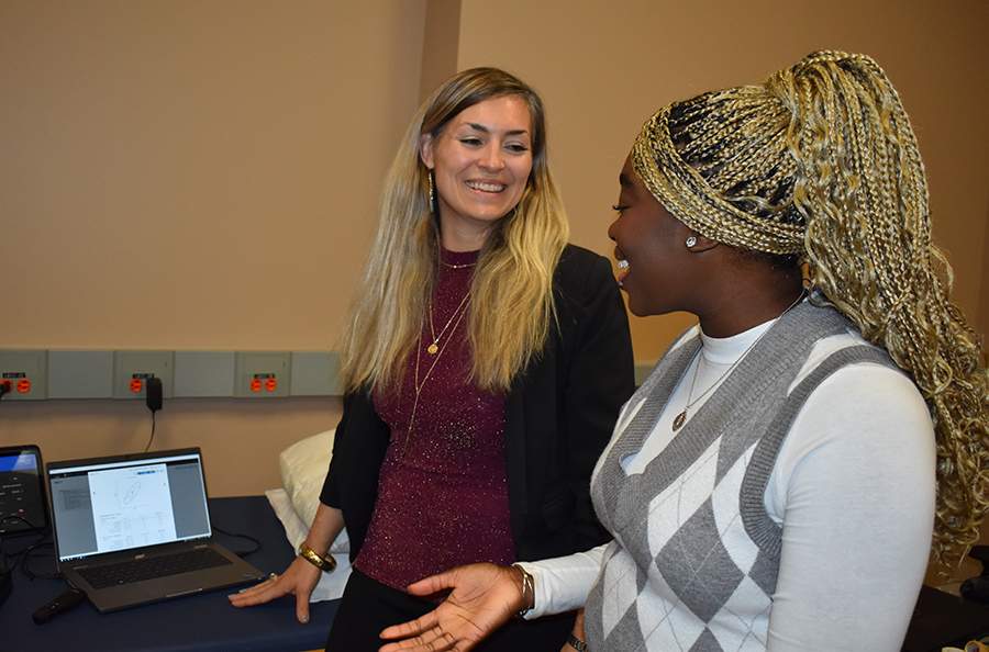 A woman laughs with a female student while they stand in front of a laptop.