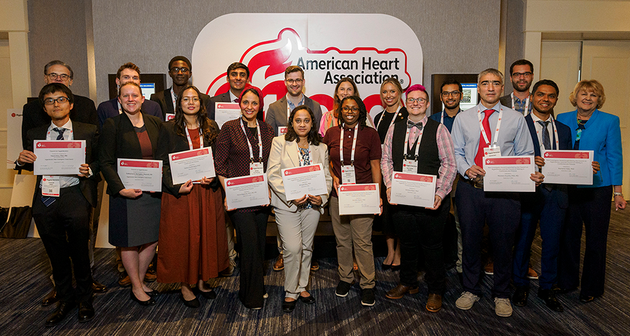 A large group of people stand in front of a sign for the American Heart Association while holding certificates for the awards they won.