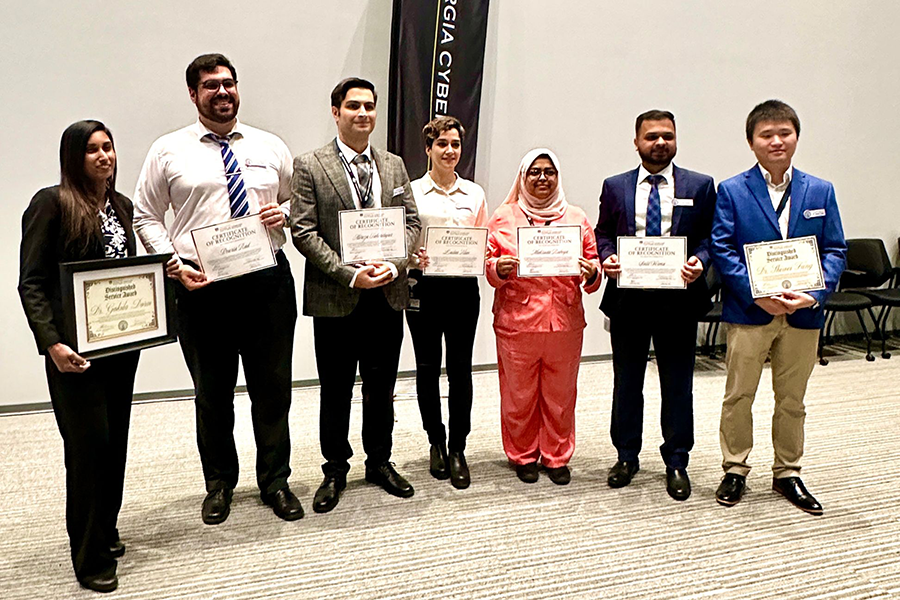 Seven people stand at the front of a large auditorium holding certificates.