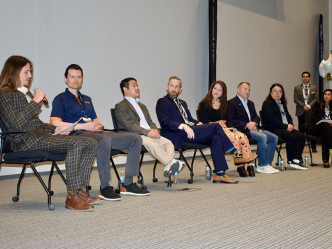 A group of people sit in chairs at the front of a large auditorium and serve as an expert panel.