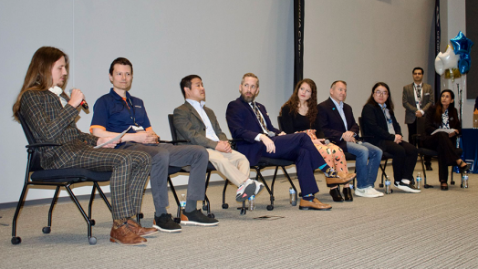 A group of people sit in chairs at the front of a large auditorium and serve as an expert panel.