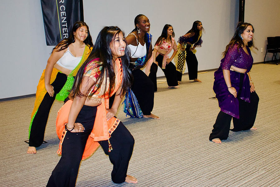 Six women dressed in culturally Indian clothing perform a dance during a ceremony.