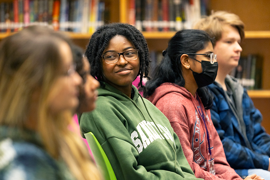 High school students sit in a library and listen to a presentation.