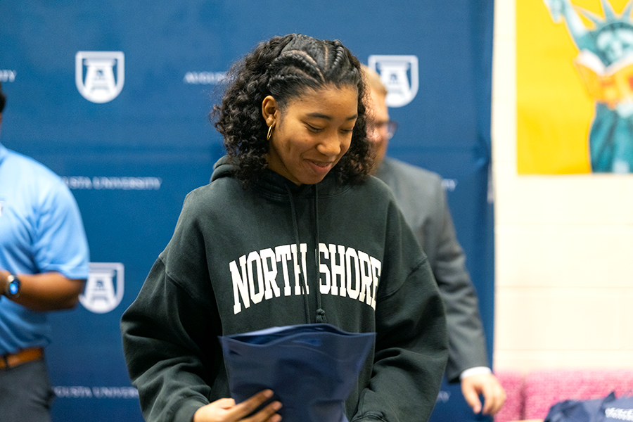 A high school senior girl smiles as she accepts a welcome packet during a ceremony for students who were admitted to a college.