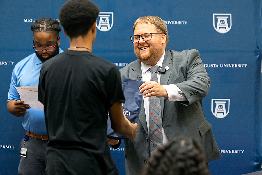 A man in a suit and tie hands a high school senior a small bag during a ceremony.