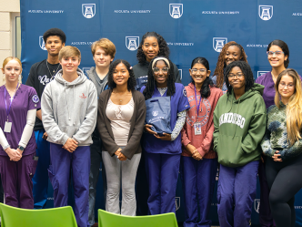 A group of 12 high school students stand for a group photo inside a modern library.