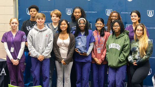 A group of 12 high school students stand for a group photo inside a modern library.