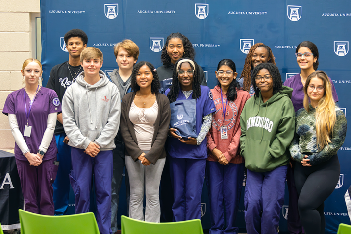 A group of 12 high school students stand for a group photo inside a modern library.