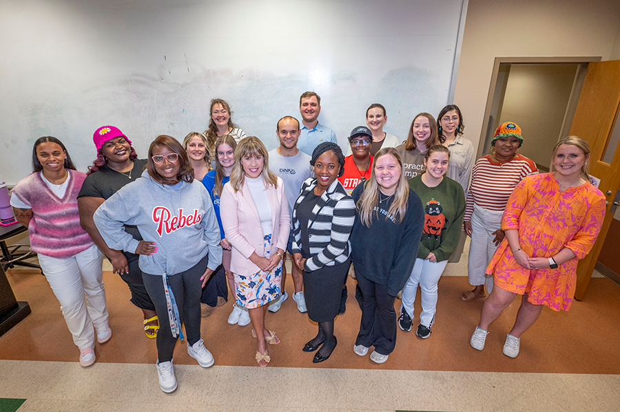 A group of college students gather around two of their professors in a large classroom.