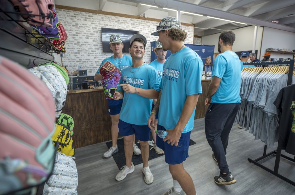 Five college baseball players stand inside a clothing store holding baseball mitts.