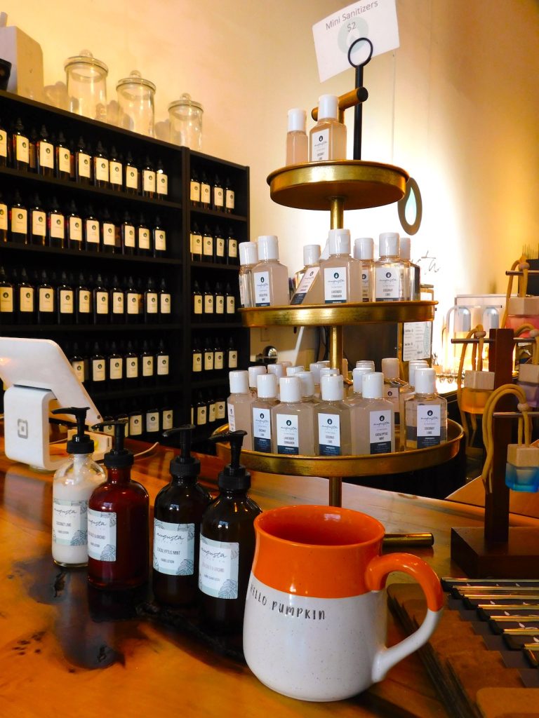 The inside of a candle shop with a shelving unit behind a counter. There are lots of jars of scented oils on the shelves.