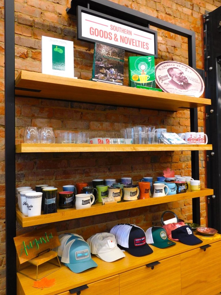 A display in a small business that includes books about the Masters golf tournament, glasses, coffee mugs, hats and more.