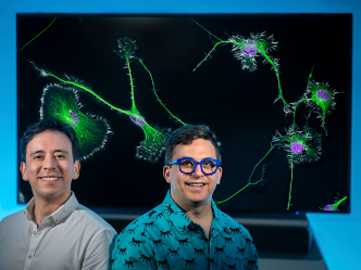 Two men stand in front of a screen. The screen features an image of several cells that can be seen under a microscope.