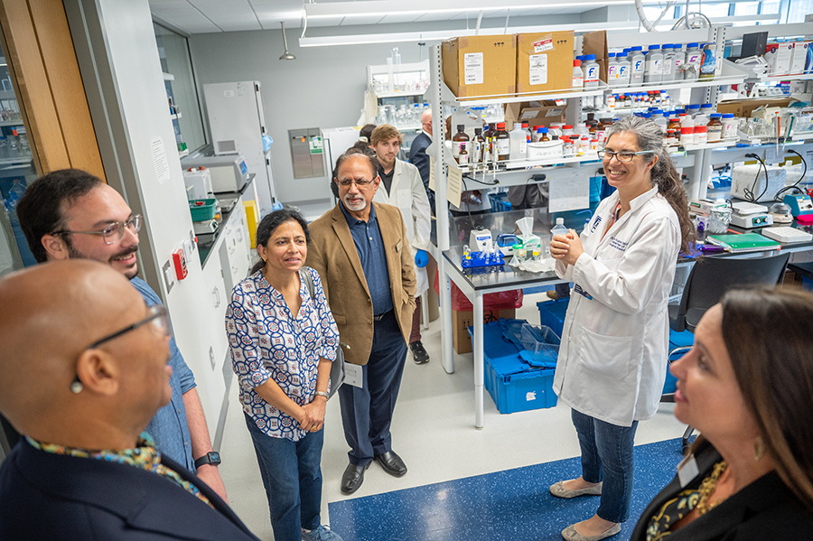 A female researcher stands in a lab and explains about her research to a group of people touring her facility.