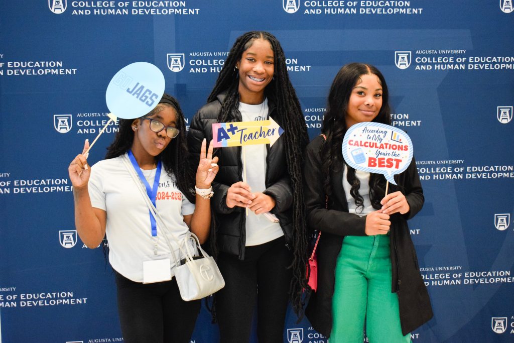 Three girls hold up silly signs as part of a photo booth and pose for a photo.