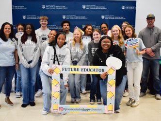 A large group of high school students pose for pictures around an oversized picture frame with cutouts of pencils around the border and the words "Future Educator."