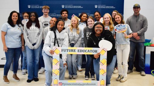 A large group of high school students pose for pictures around an oversized picture frame with cutouts of pencils around the border and the words "Future Educator."