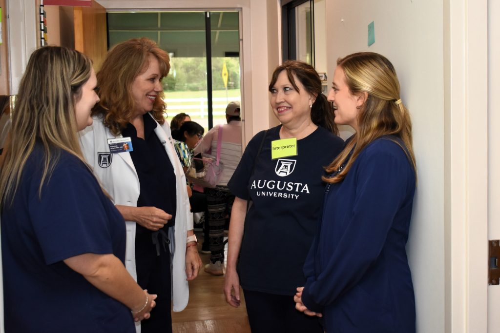 A female nurse speaks with two nursing students and an interpreter in a hallway as they wait for their patient.