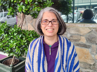 A woman in glasses stands outside of a business.