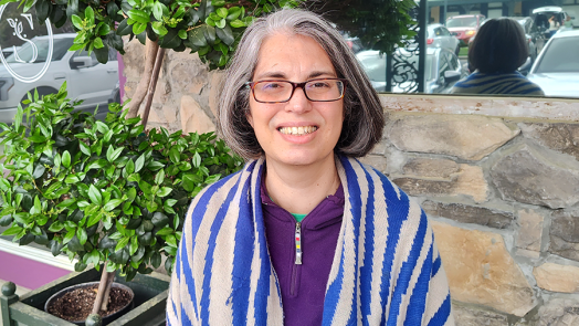 A woman in glasses stands outside of a business.