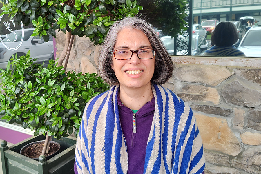 A woman in glasses stands outside of a business.