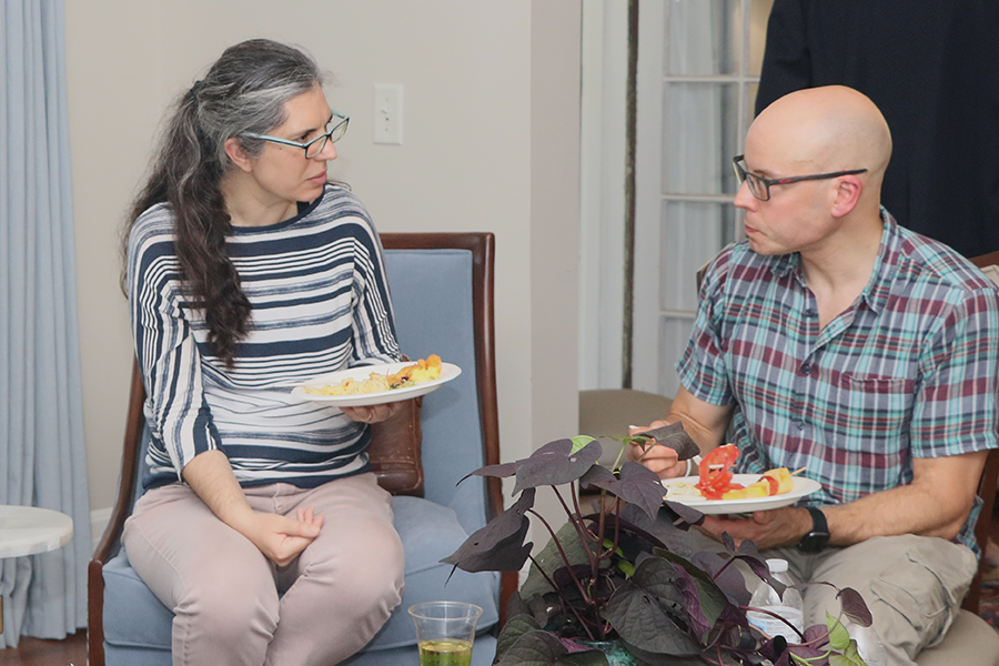 A man and a woman sitting and talking. Each is holding a plate of food.