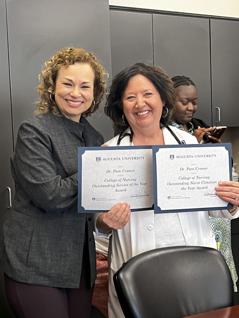 A woman holds up a pair of certificates while another woman smiles.