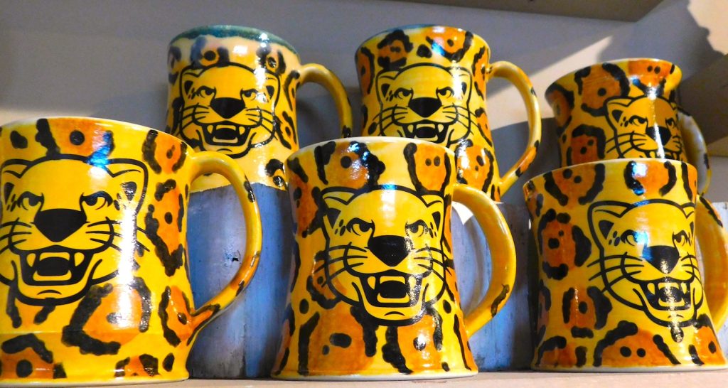 Hand-made ceramic mugs painted with a pattern mimicking a jaguar's spots and featuring a mascot head depicting a jaguar.