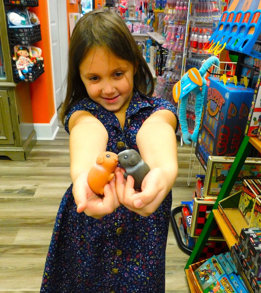 A little girl holds two fake hamsters inside a toy store.