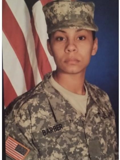 A woman in a military uniform posed in front of a flag. 