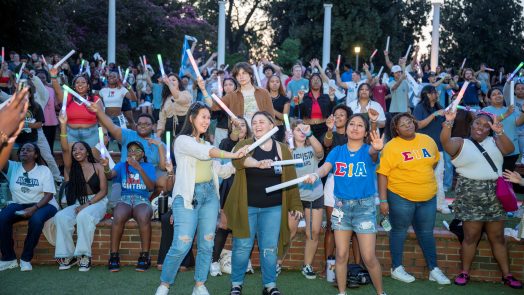 Many college-aged students stand outside holding glow sticks.