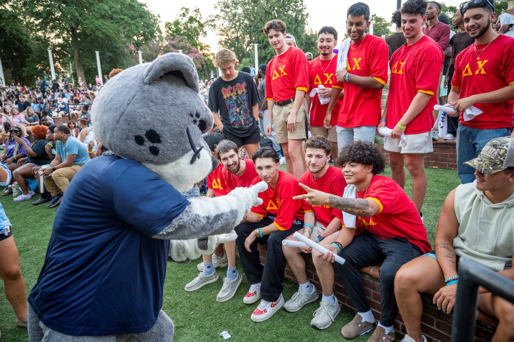 A group of men face a jaguar mascot.