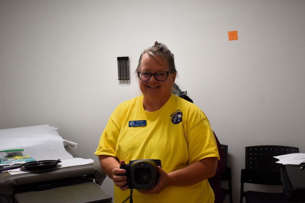 A woman stands in a medical clinic holding a camera.