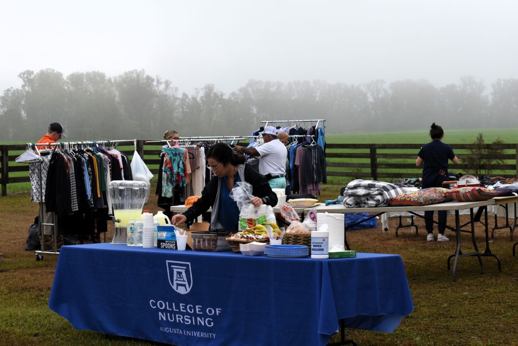 Tables and clothing racks are spread out around a lawn as people look at the clothing items.