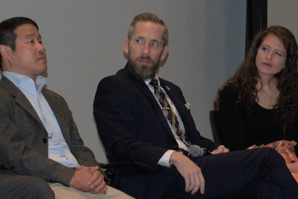 Two men and a woman sit at the front of a large auditorium.